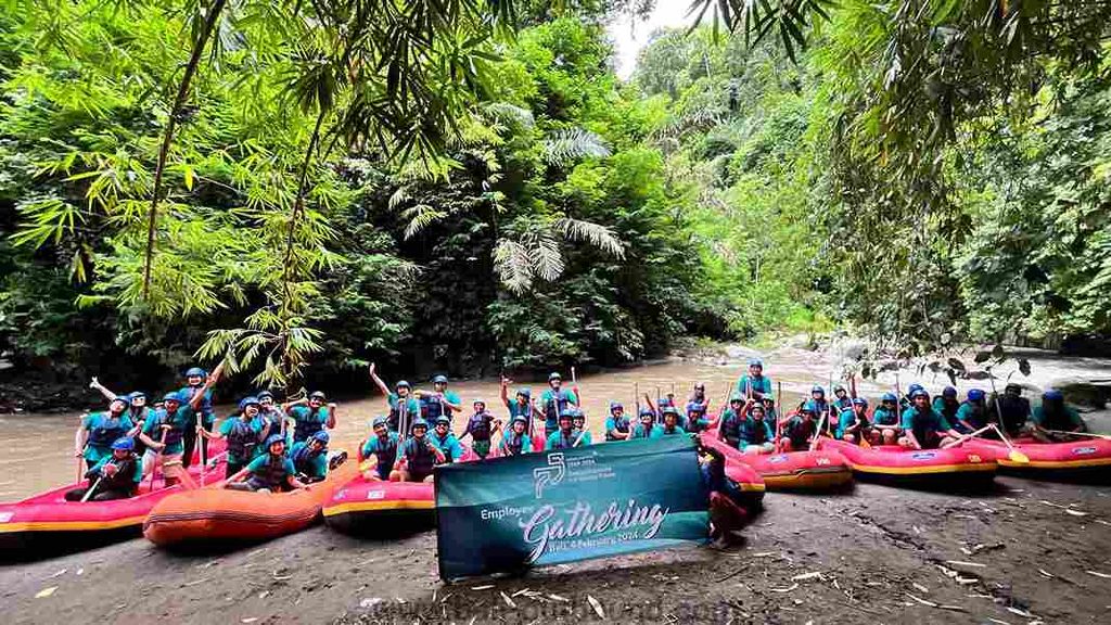 Tim peserta bekerja sama mengarungi jeram Sungai Ayung dalam aktivitas rafting dan team building di Bali.